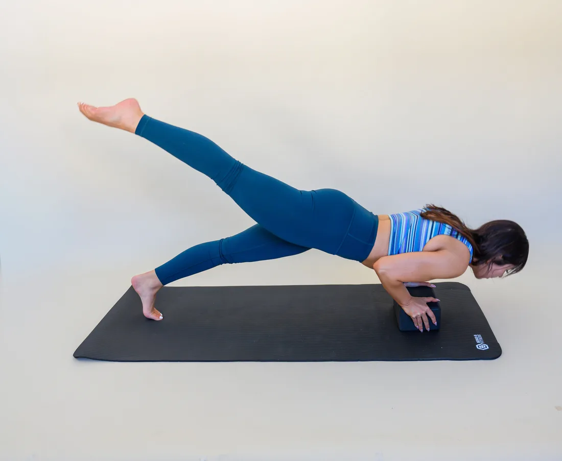 Abby on a mat in a forearm plank with one leg lifted high behind her, demonstrating mat pilates